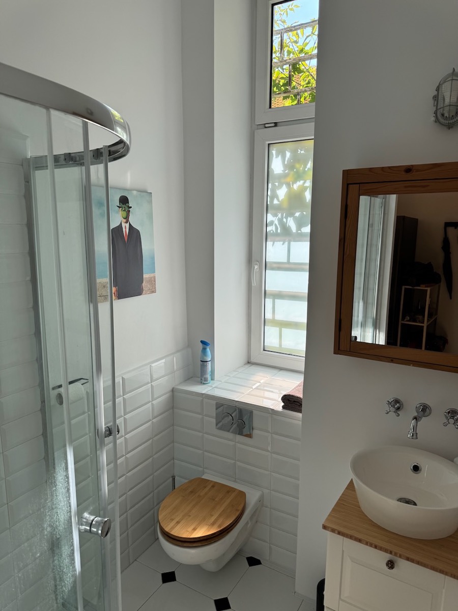 White-tiled bathroom with corner shower, vessel basin, bamboo-seat toilet and tall window