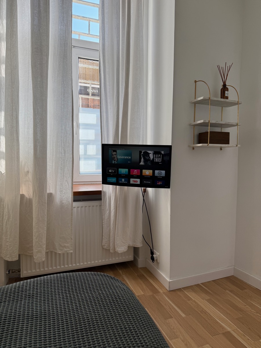 Second television on a swing arm by the bedroom window, linen curtains and a brass and marble wall shelf