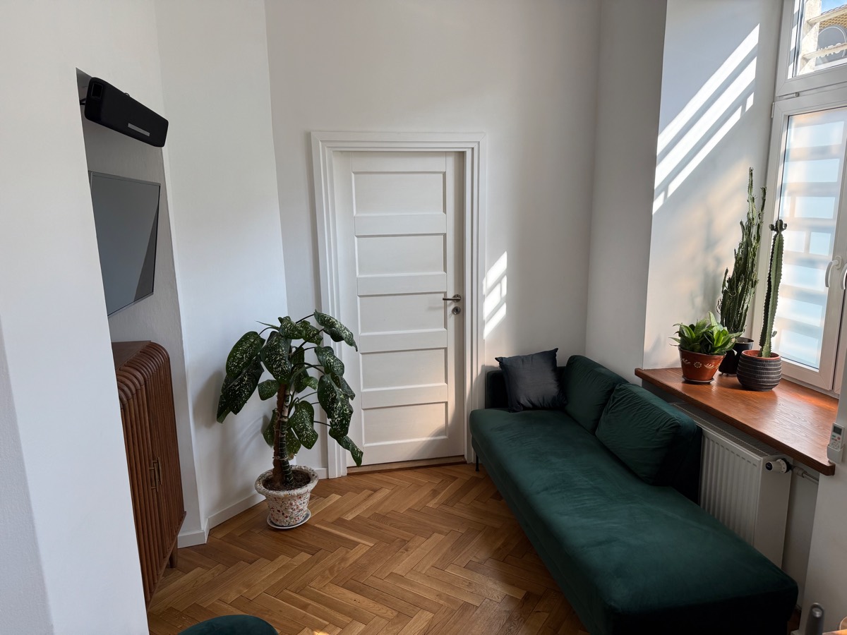 Living area with a green velvet daybed under the window and a wall-mounted TV above a fluted walnut cabinet