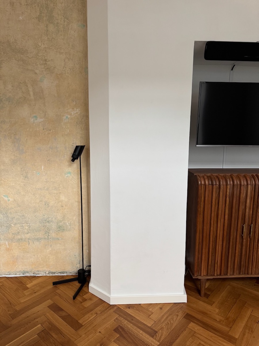 Close view of the raw plaster wall texture lit by a black floor lamp