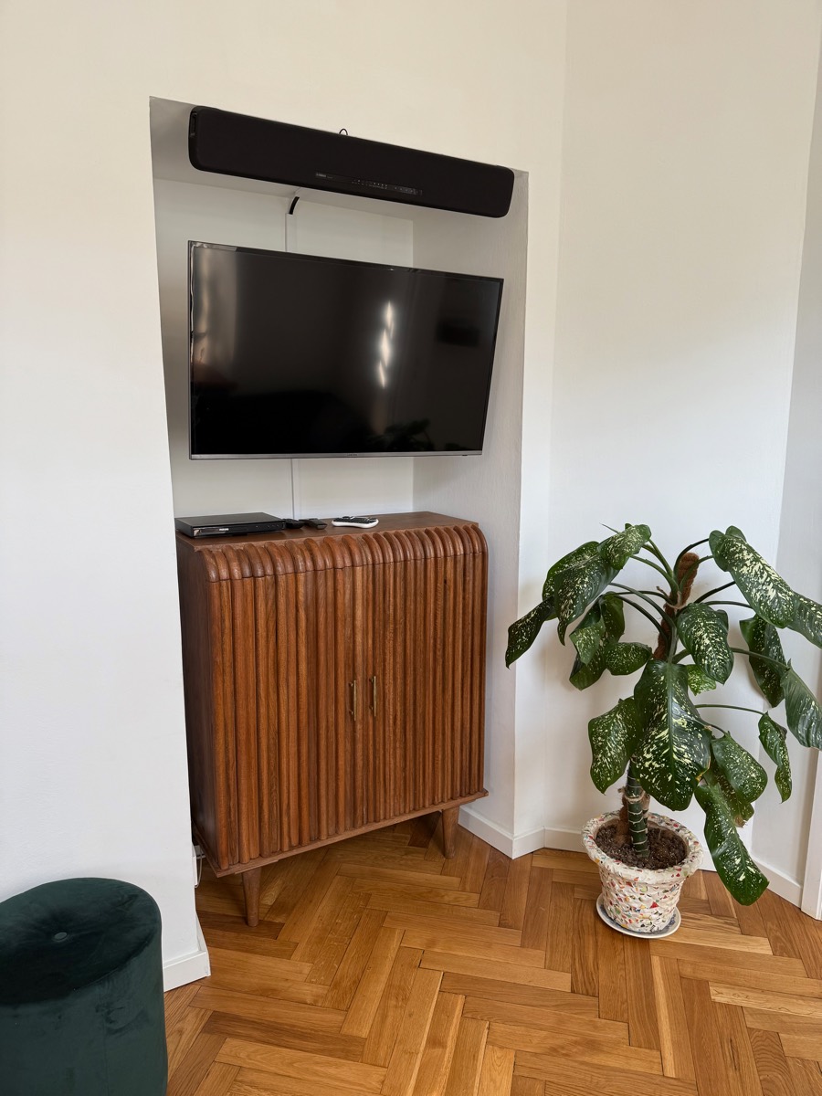 Wall-mounted TV and soundbar above a fluted walnut cabinet, dieffenbachia on the herringbone parquet