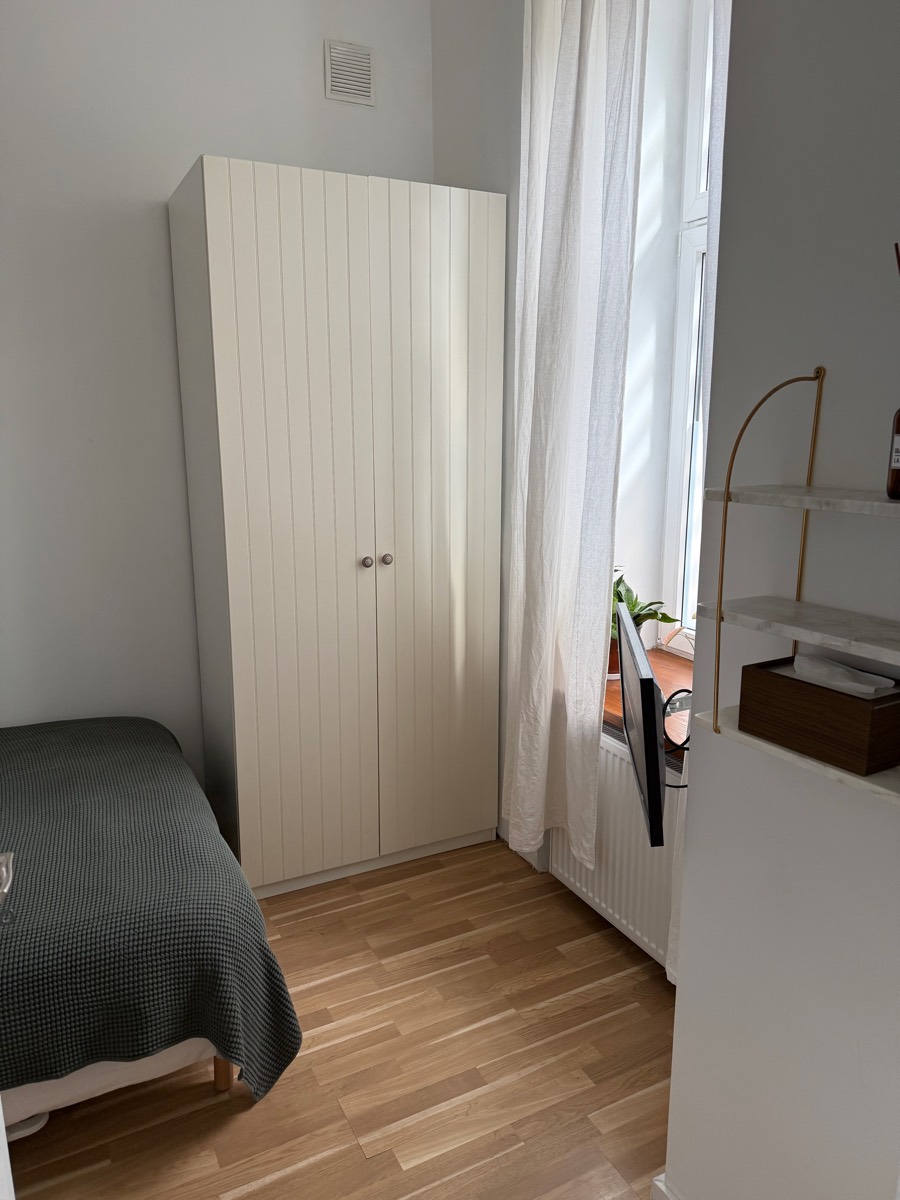 Bedroom with a tall ribbed white wardrobe, sage waffle bedspread and a linen curtain at the window